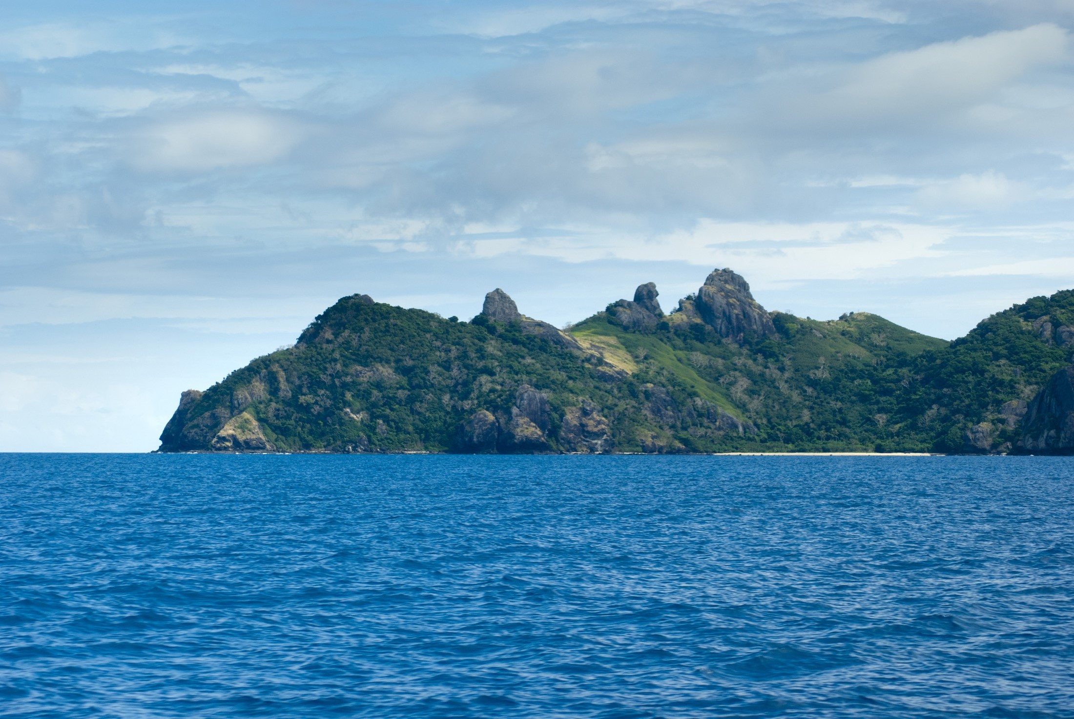 an image of View across open blue ocean while cruising offshore of Yasawa Islands Fiji showing the rocky topography of these beautiful tropical islands