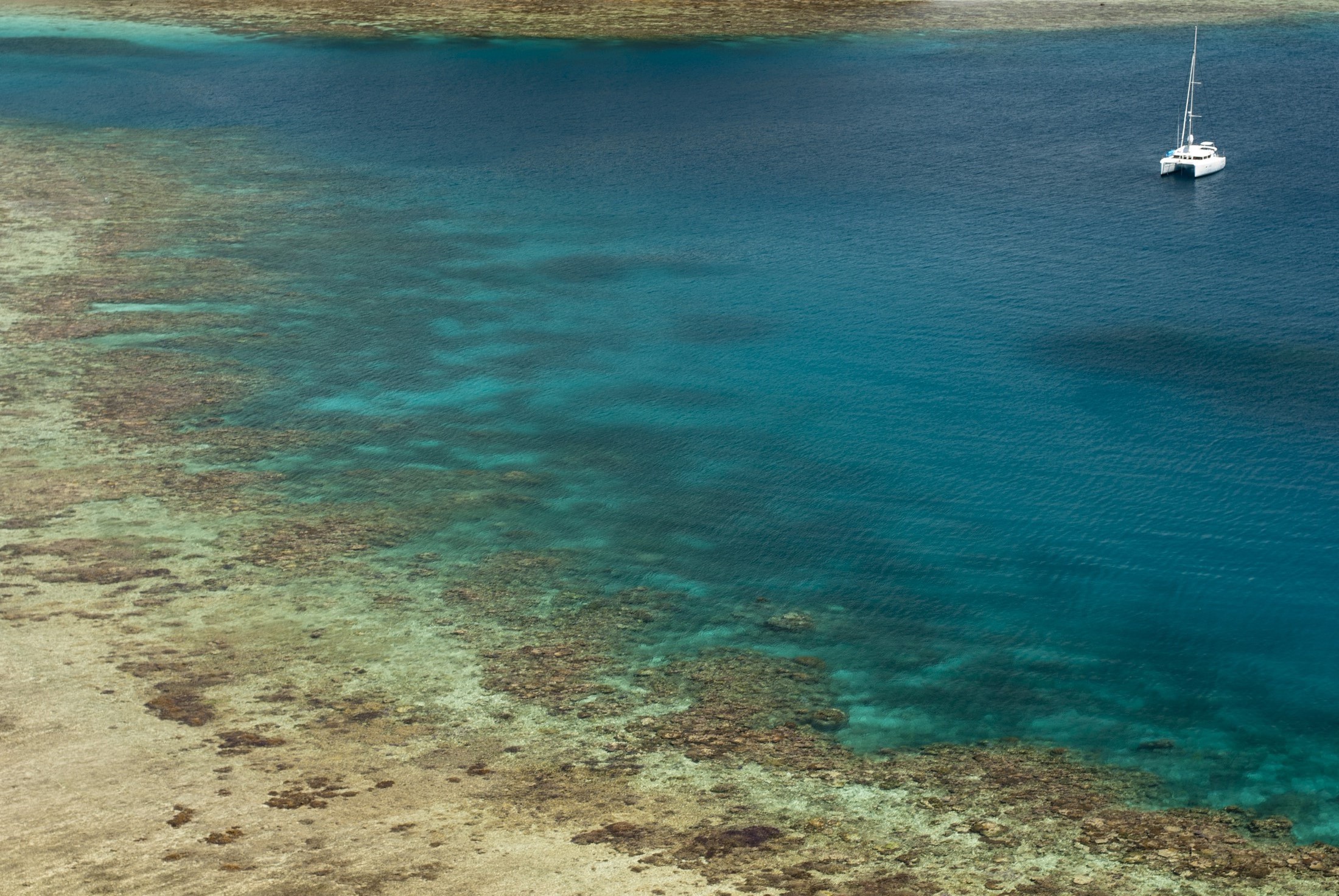 an image of panoramic view of fringing coral reefs and a sailing catamaran at anchor