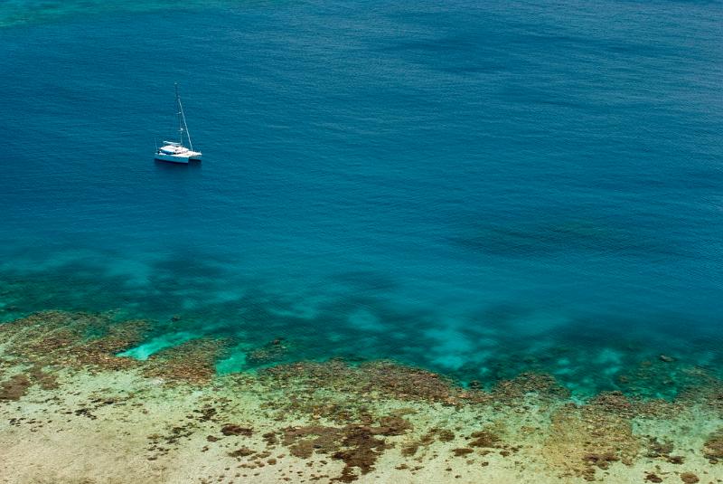 Blue ocean and crystal clear shallows off Yasawas Island, Fiji with a yacht passing close to shore and copyspace