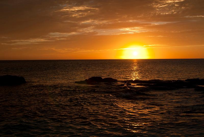 Vivid sunset over the calm ocean as the orange orb of the sun just dips below the horizon