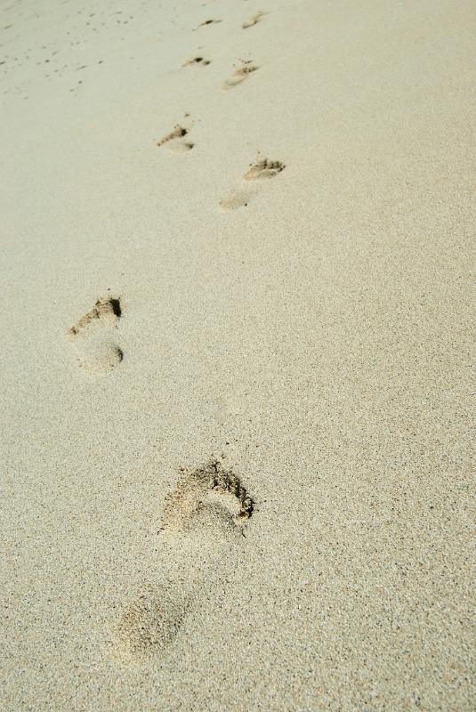 Barefoot footprints on a sandy beach leading away from the camera