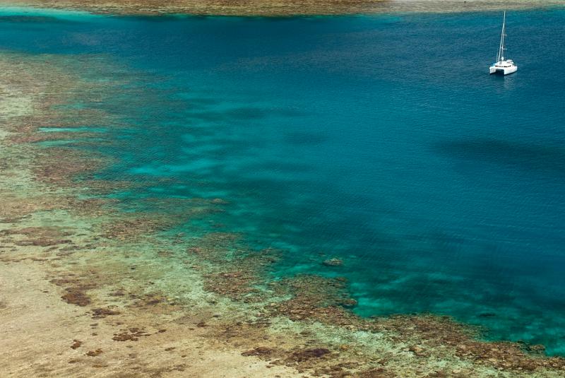 panoramic view of fringing coral reefs and a sailing catamaran at anchor
