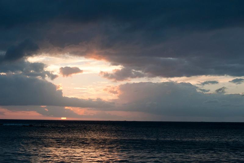 Setting sun over the ocean shing through a break in the heavy cloud cover with a delicate pink glow illuminating the water