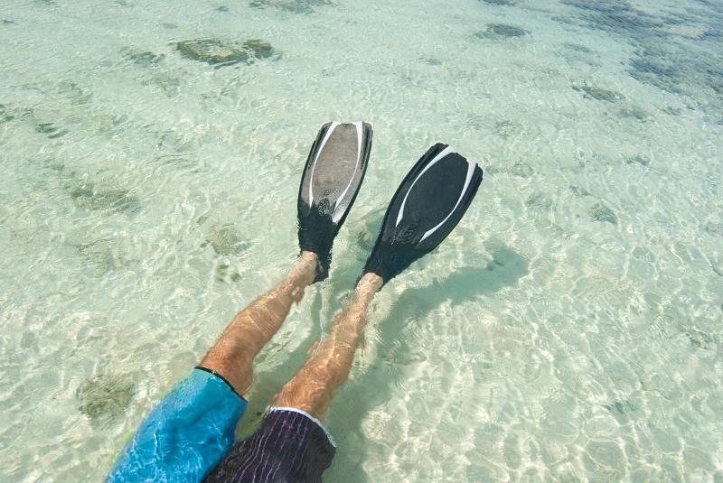 Man lying on his back wearing a pair of fins snorkeling in clear tropical water off a Fijian island