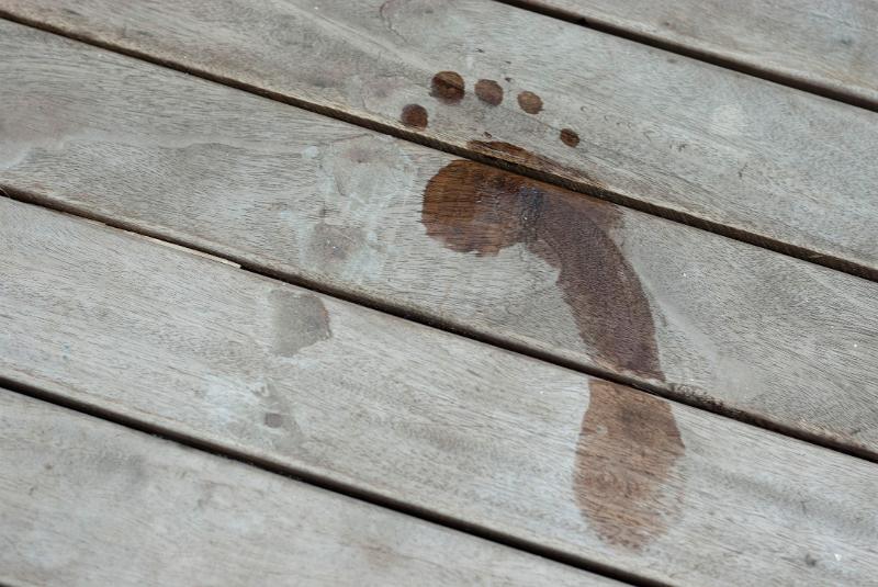 Wet footprint on a wooden board left by a swimmer exiting the water on vacation