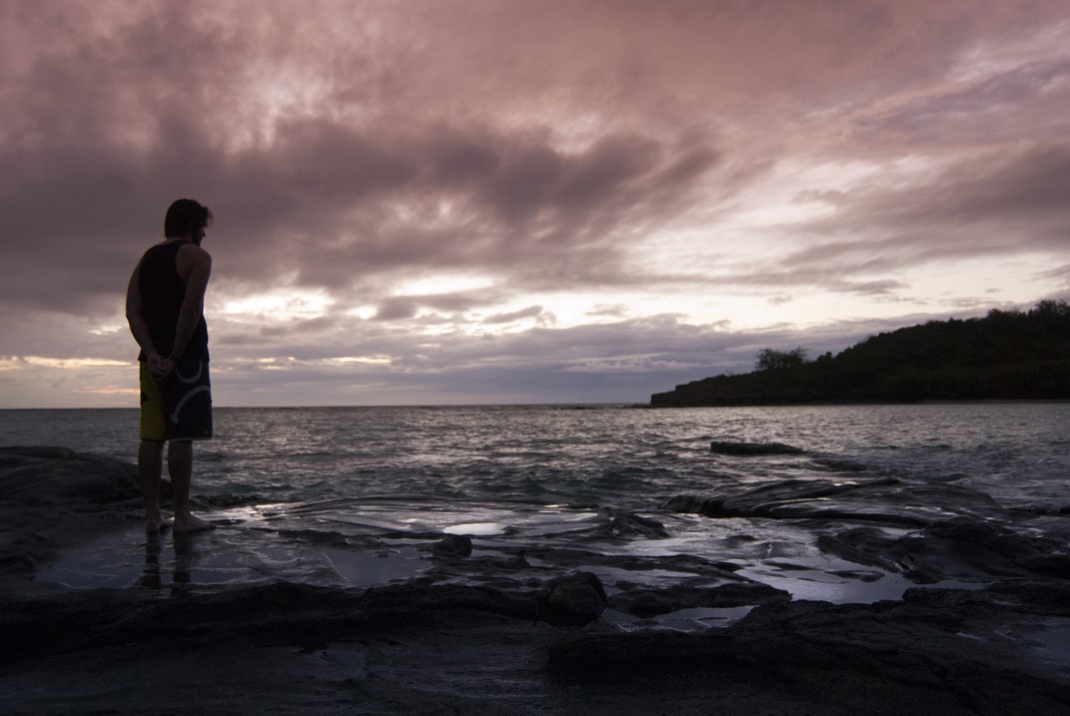 an image of Man in silhouette standing on the seashore watching a marine sunset with clouds tinted a lilac purple