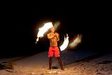 Fijian fire dancer performing with flaming branches on a sandy beach twirling them around his naked torso