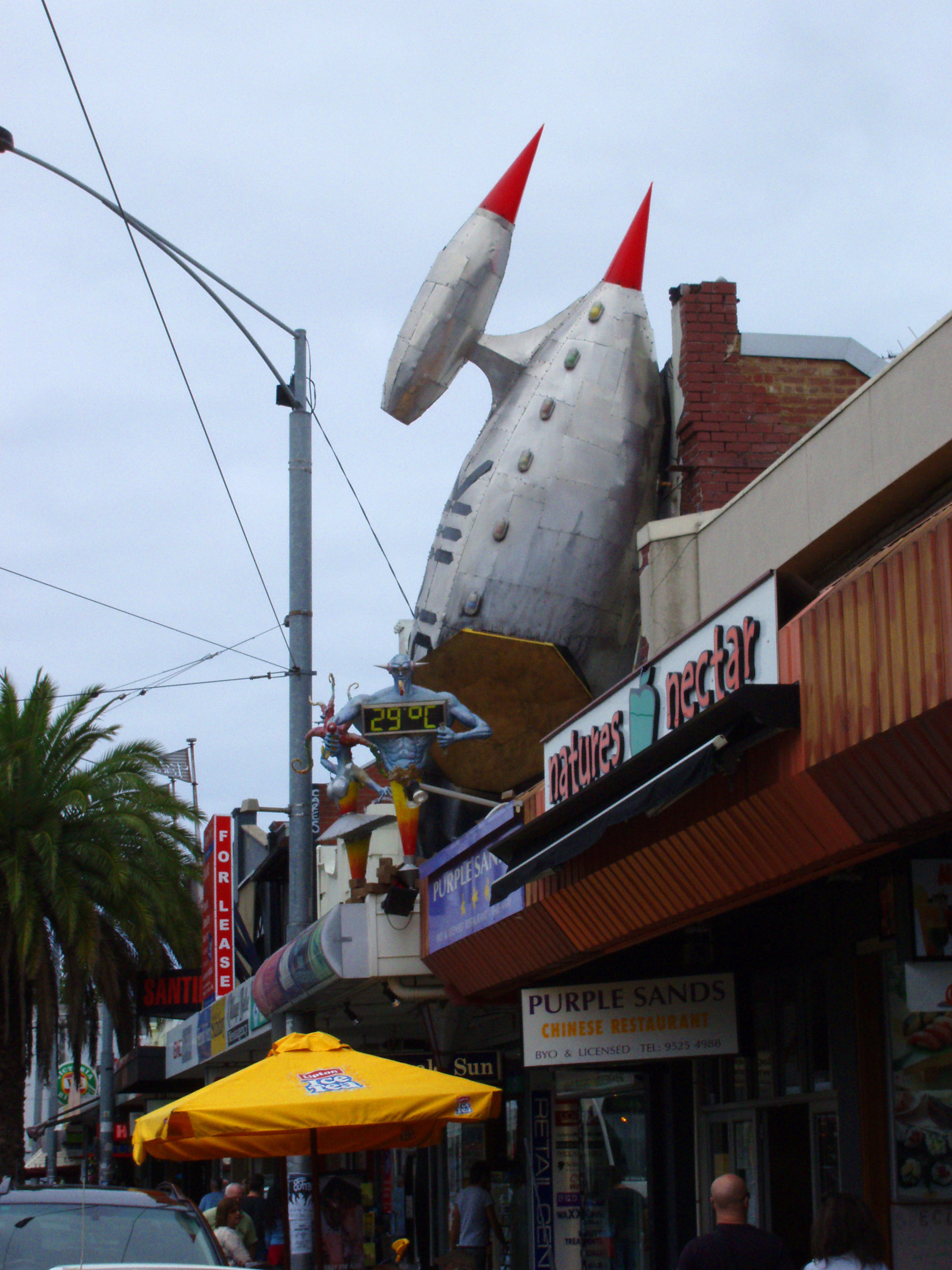an image of Huge Space Rocket with Muscular Man Sculpture on Street Cafe in St. Kilda, Melbourne.