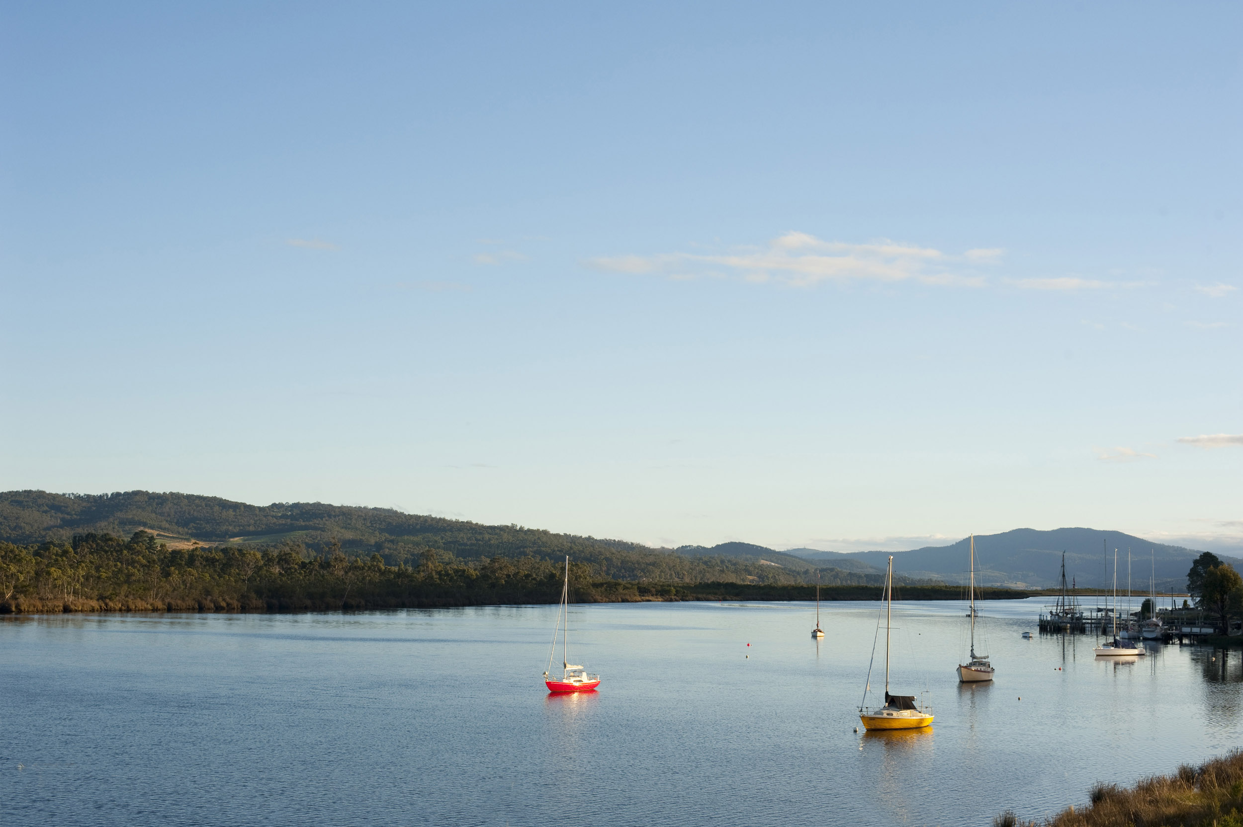 an image of Boats moored on the Huon River in Tasmania are lit by the warm light of the sunset.