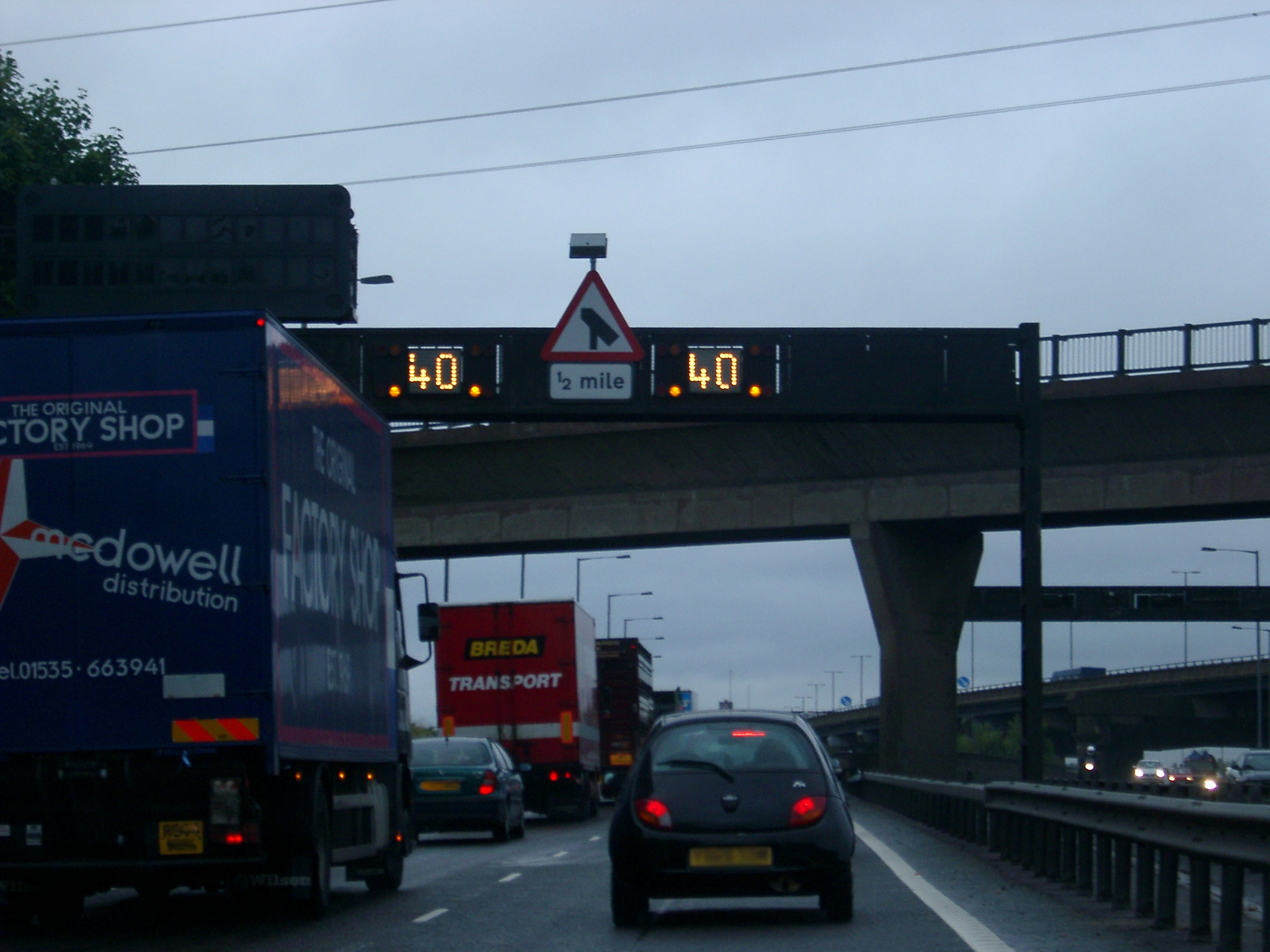 an image of Traffic on Multi Lane Highway Passing Beneath Overpass on Grey Day from Driver Perspective