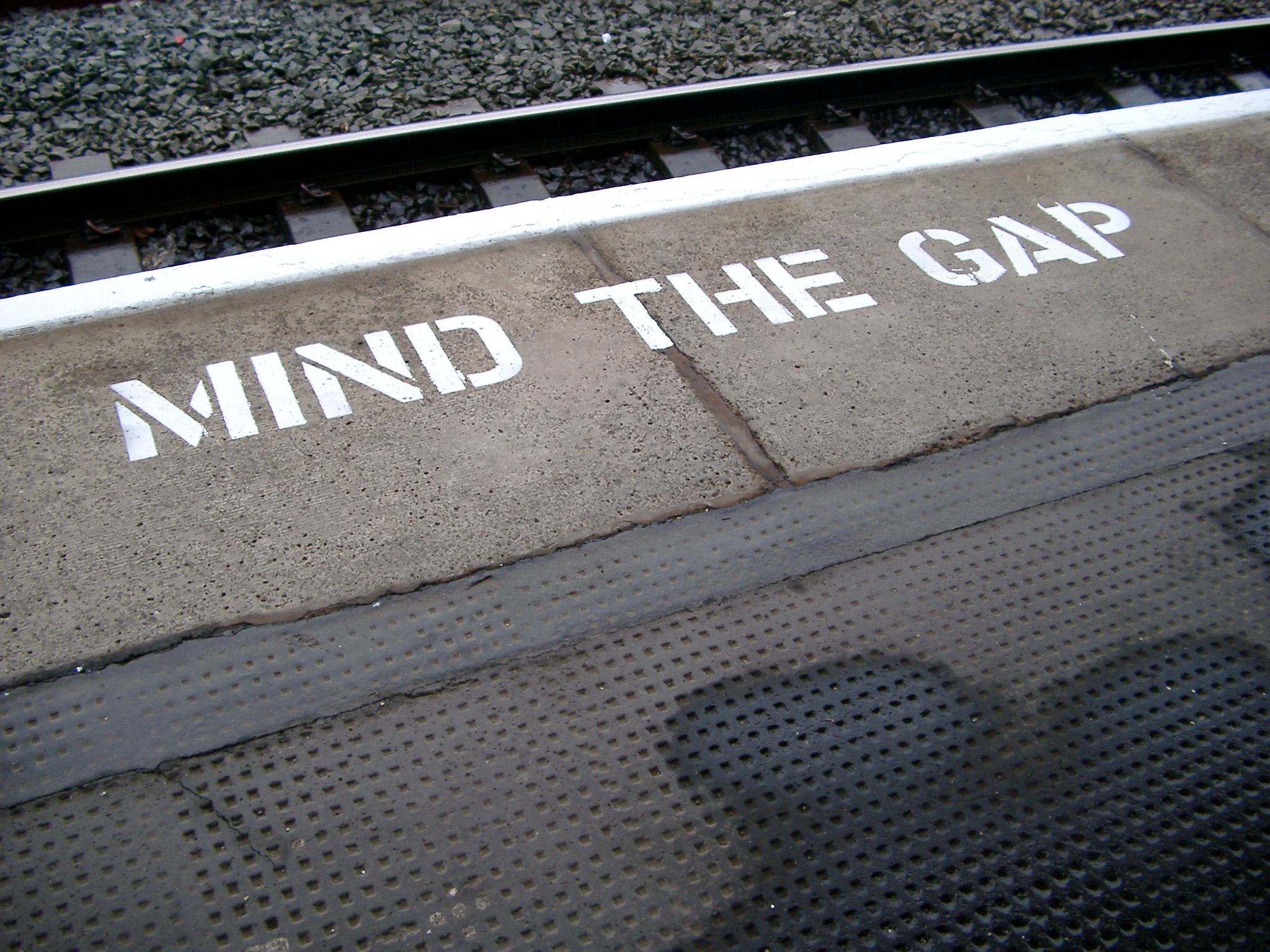 an image of Platform edge at a train station with the warning - Mind The gap - painted in white on the edge of the tracks