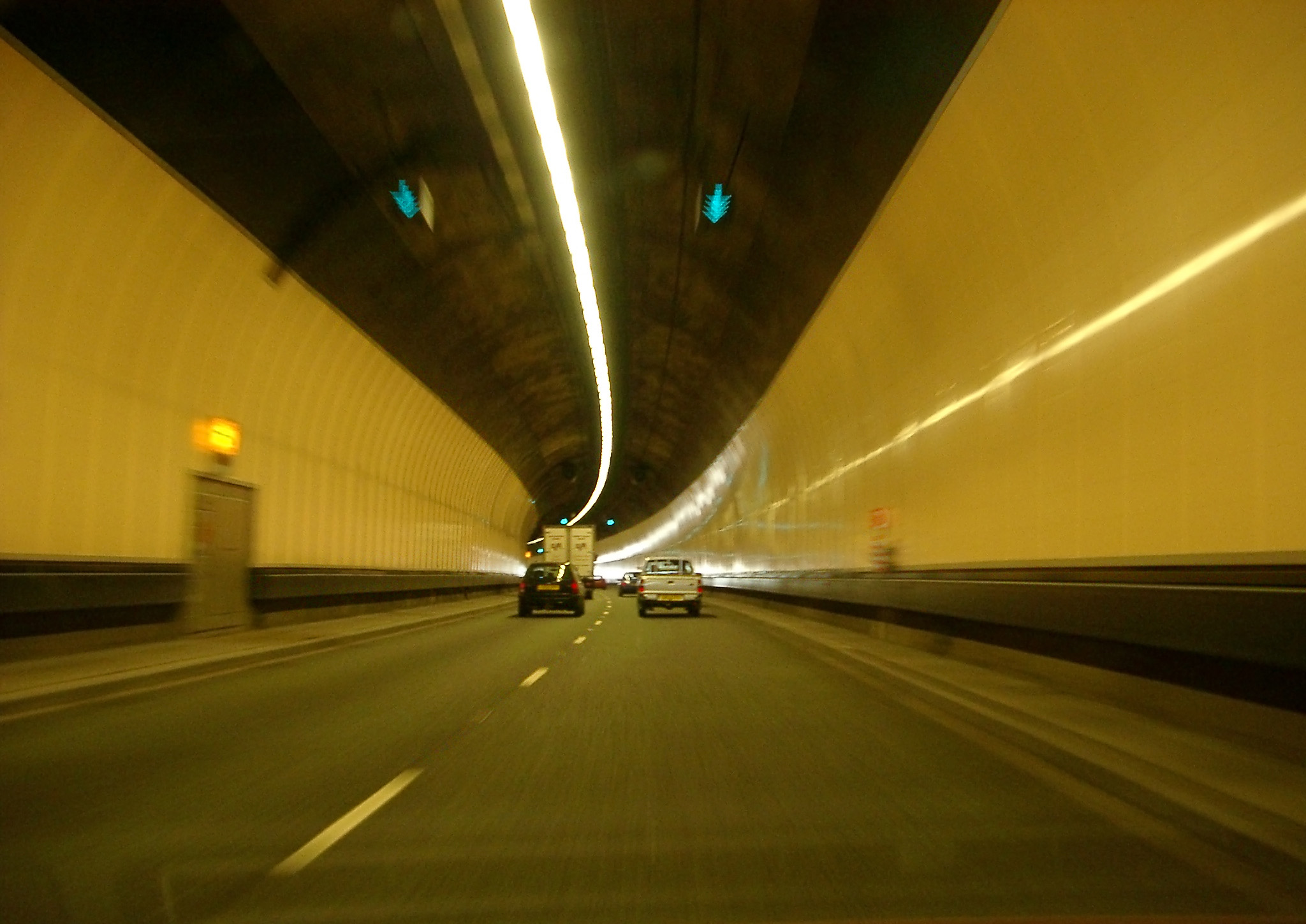 an image of Interior of an enclosed road tunnel with a dual lame highway and cars and vans travelling away from the camera approaching a bend
