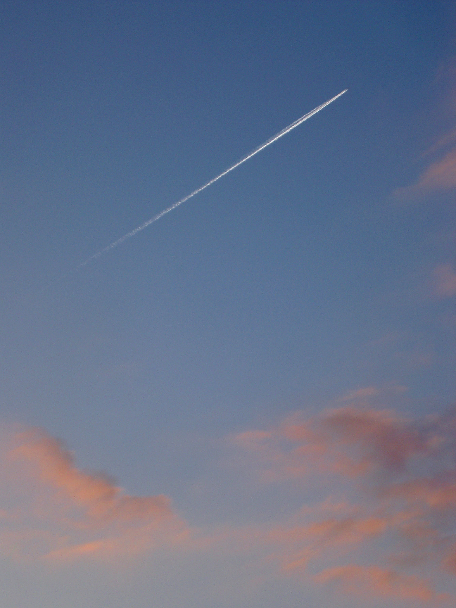 an image of Jet trail or contrail in an evening sky with colorful pink clouds of condensed water vapor from a passing aircraft