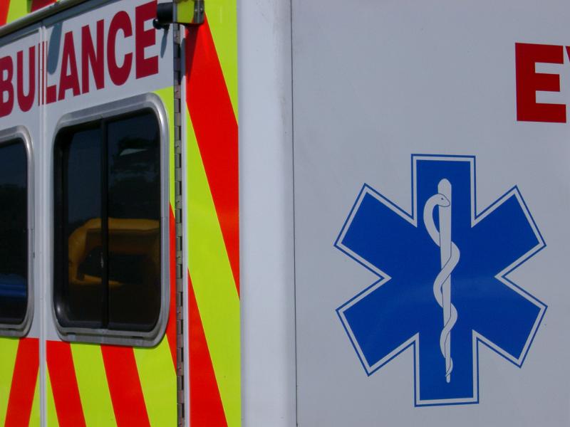 Ambulance showing the snake and staff symbol of the emergency medical service with a portion of the rear door and red and yellow neon chevron visible