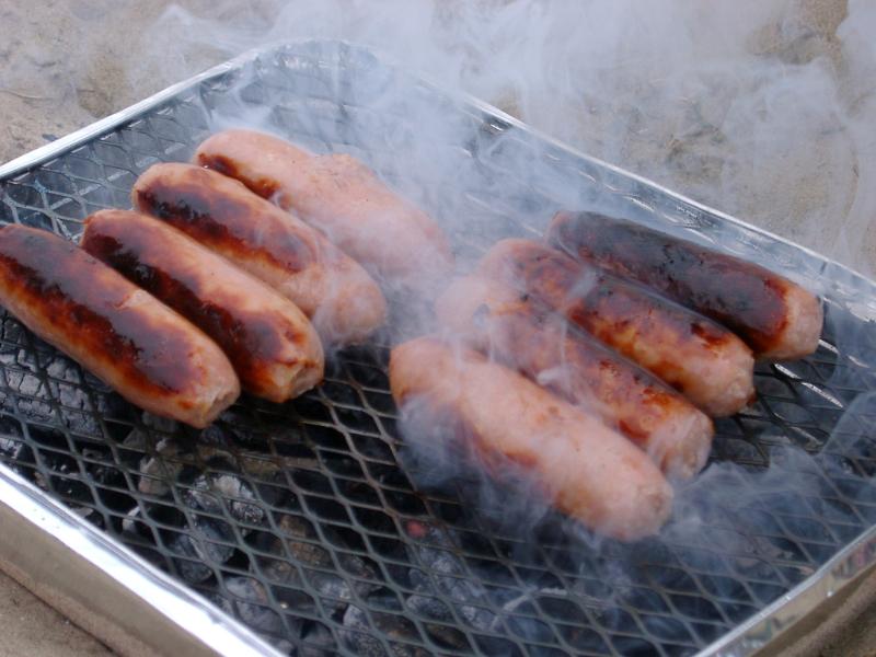 Sausages grilling on a BBQ over smoking hot coals in a healthy outdoor lifestyle concept