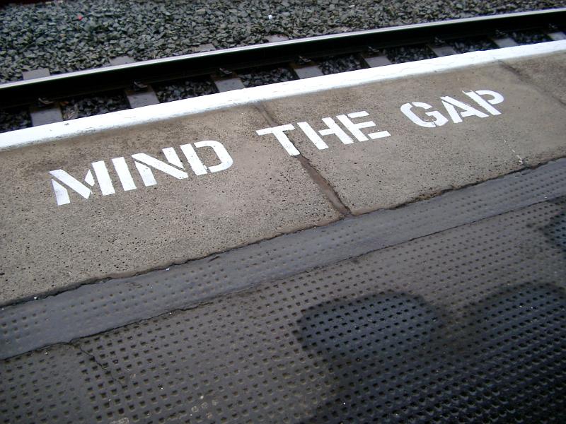 Platform edge at a train station with the warning - Mind The gap - painted in white on the edge of the tracks