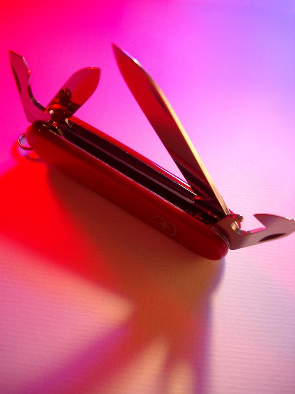 Swiss army knife Swiss army knife opened to display the tools and gadgets in colorful red, pink and purple light with copyspace