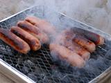 Sausages grilling on a BBQ over smoking hot coals in a healthy outdoor lifestyle concept