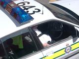 High angle view of a police car with the patrol car number and blue lights visible on the roof and a police officer sitting in front