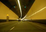 Interior of an enclosed road tunnel with a dual lame highway and cars and vans travelling away from the camera approaching a bend