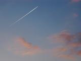 Jet trail or contrail formed by condensation of vapor and ice particles streaking through a blue sky at sunset with colorful pink clouds