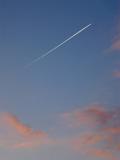 Jet trail or contrail in an evening sky with colorful pink clouds of condensed water vapor from a passing aircraft