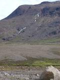 Desolate volcanic mountain landscape in Iceland with a river flowing down a mountain peak onto the plains below