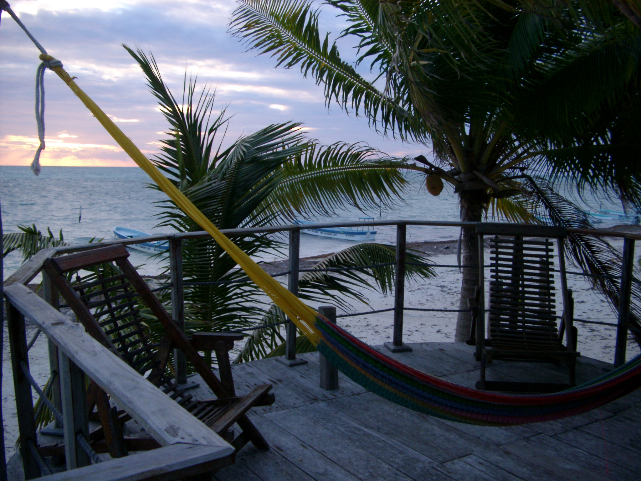 an image of Hammock on a wooden deck overlooking the ocean with tropical palm trees in a travel and summer vacation concept