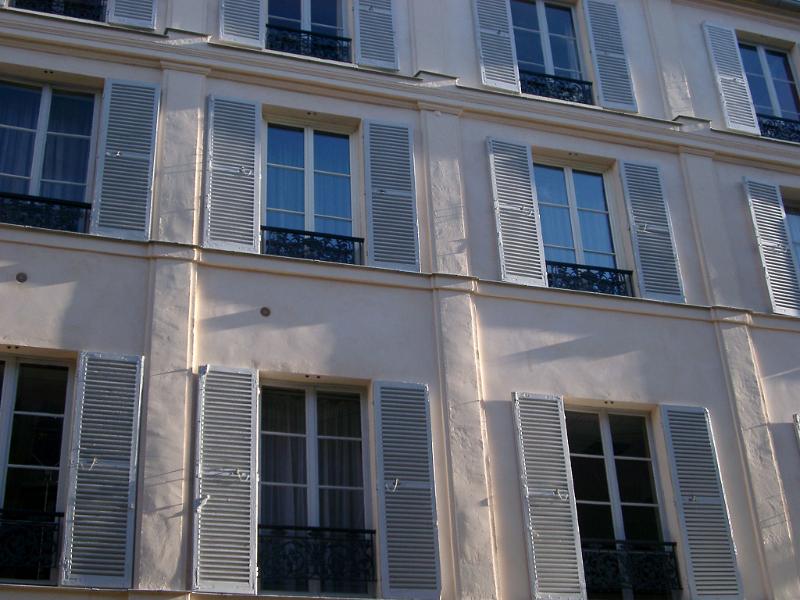 View of the facade of a Paris townhouse with slatted wooden window shutters on the tall windows