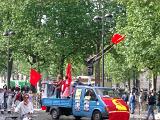 Men with Flags on Vehicle with Random People on Ground During May Day Parade. Isolated on Tall Green Trees.