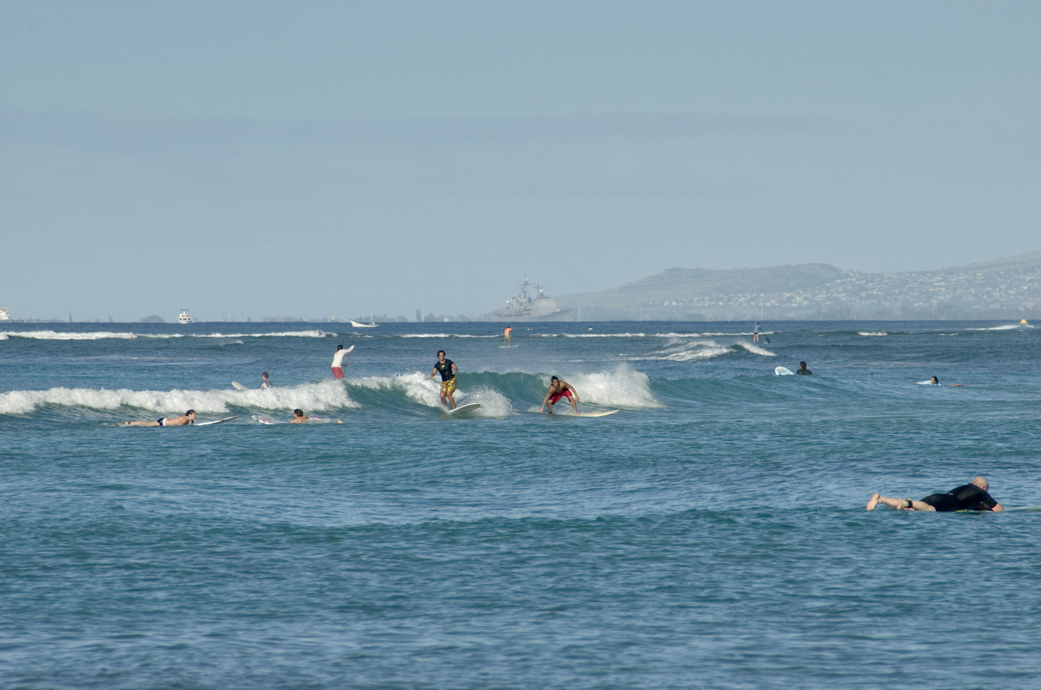 an image of Few Tourists Surfing at Blue Water Waikiki Beach. Isolated Light Blue Gray Sky Background.