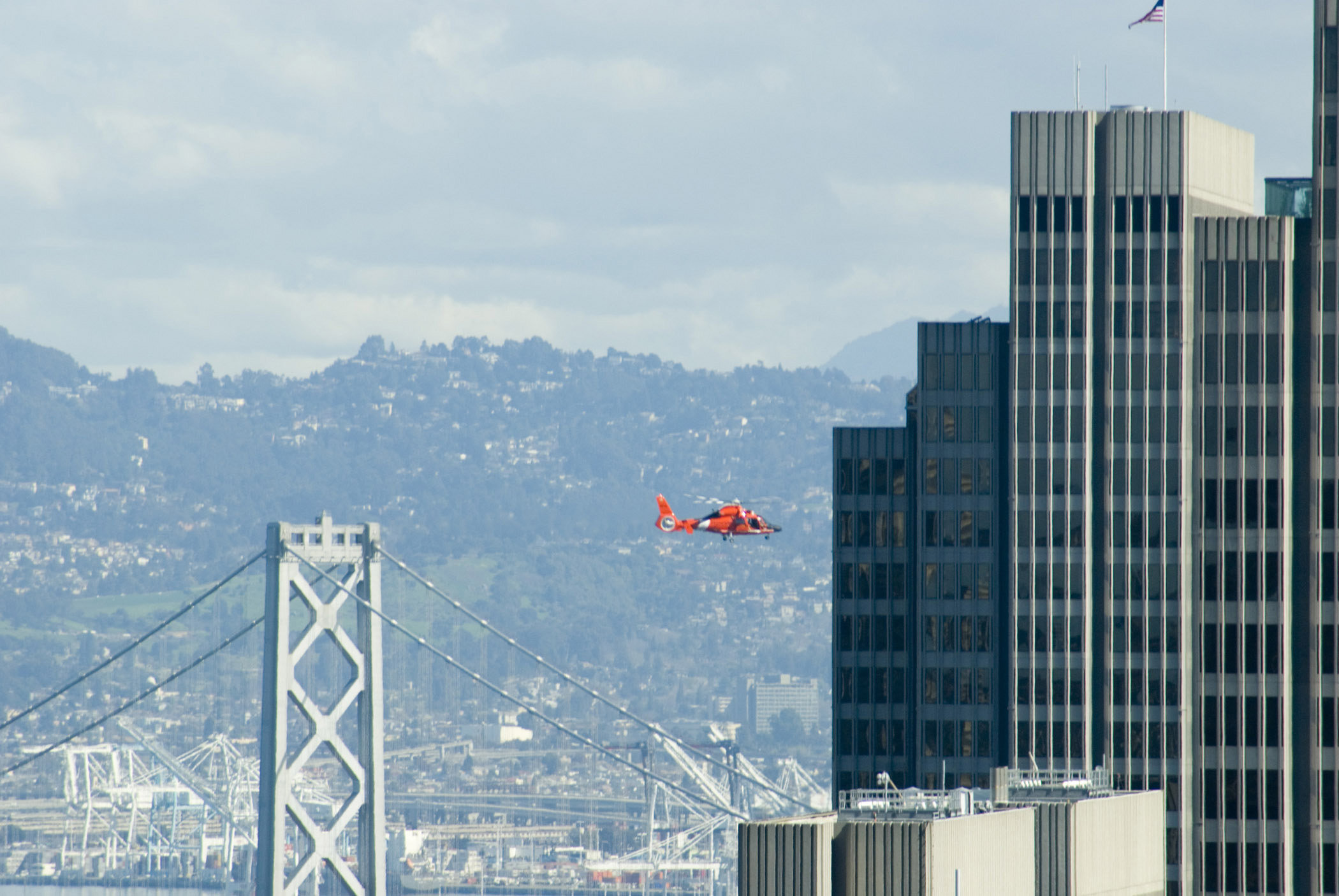 an image of Solo Flight Passing Famous Bay Bridge and High Rise Buildings at San Francisco. Captured with Mountains View Afar.