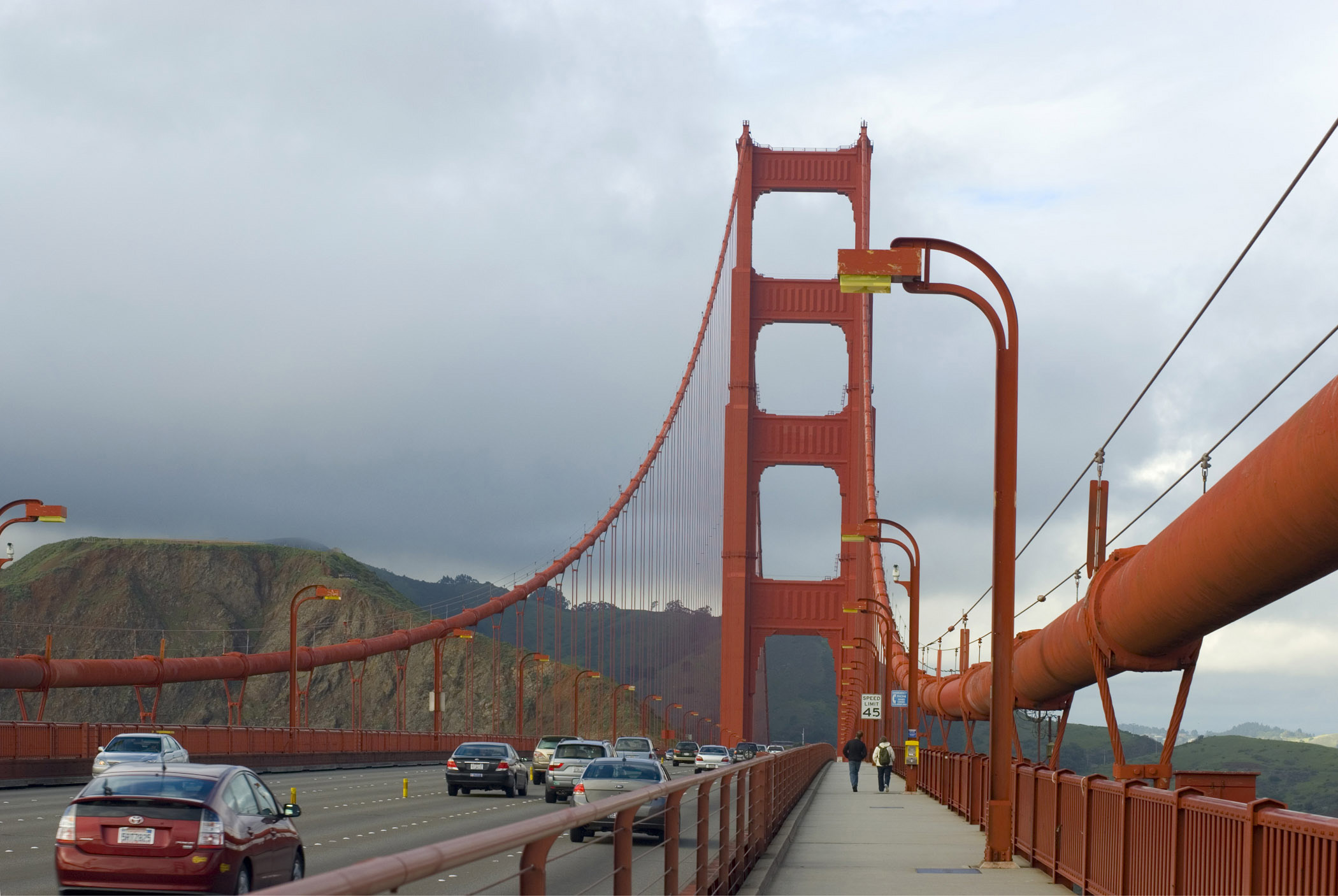 an image of Walk Along the Golden Gate Bridge San Francisco. Captured with Mountains in the distance with a Stormy Sky Background.