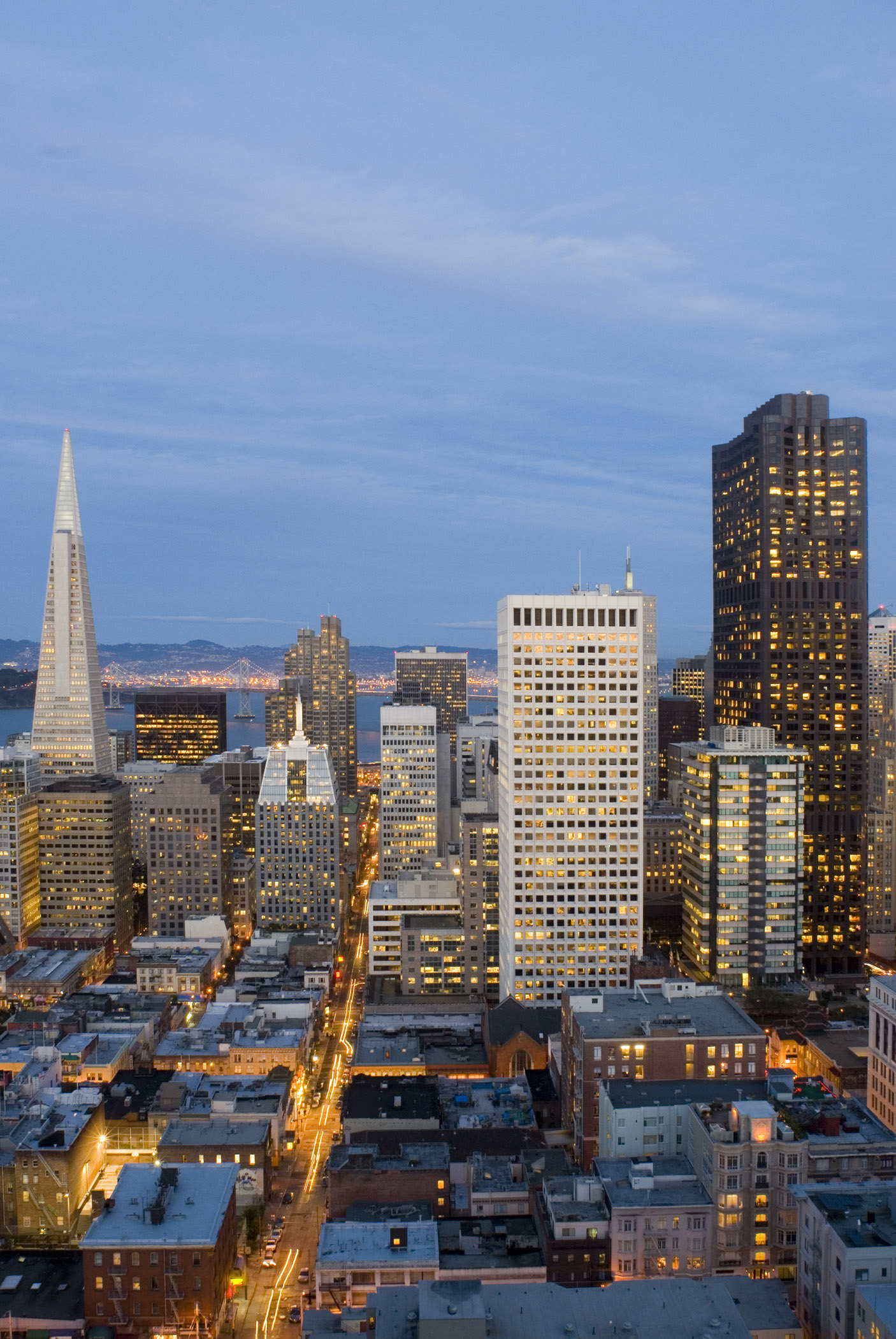 an image of San Francisco, California, at night with a view over rooftops to the CBD with its modern skyscrapers and high-rise buildings illuminated at twilight