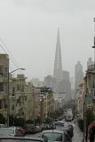 Rainy day in San Francisco, California, with a view down a steep residential hill towards the CBD and a spire through the mist