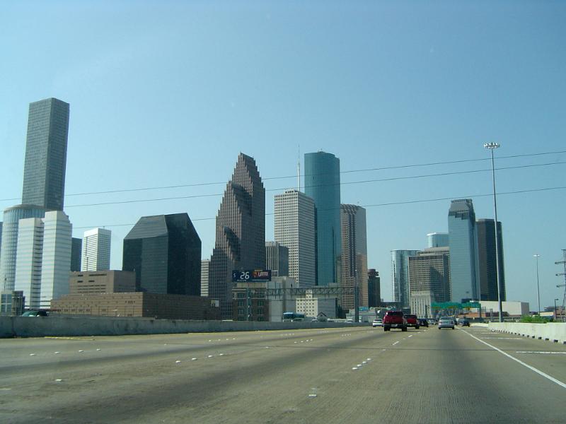 Attractive Architectural Buildings Along Freeway on Light Blue Sky Background.