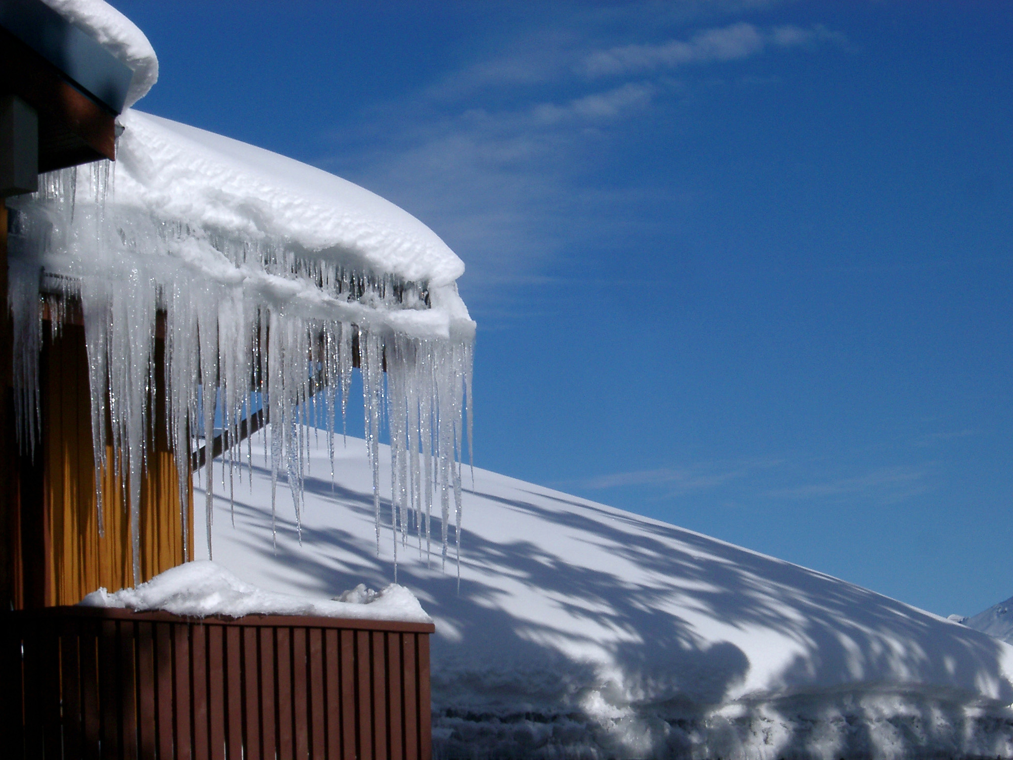 an image of Winter holiday cabin in the Alps with a row of icicles hanging from the roof on a sunny blue sky winter day