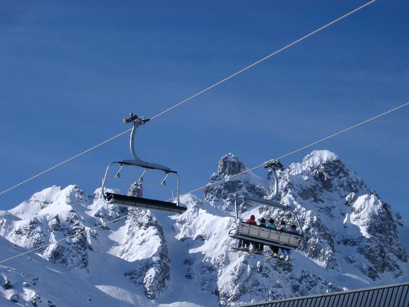 Tourists Riding High Cable Car on a Snow Mountain on Light Blue Sky Background.