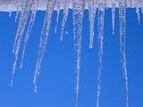 Row of long icicles hanging from the edge of a snow covered roof against a clear crisp sunny blue winter sky