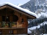 Snow on Rooftop at Vintage Wooden Alpine Lodge Building with Huge Mountain Background.